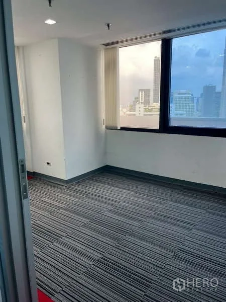 Office Space for rent - Small office room with striped carpet tiles and a large window overlooking the city.