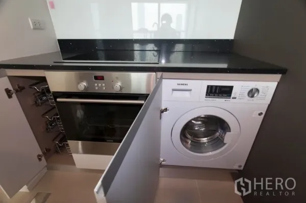 คอนโด ให้เช่าหรือขายในKhlong San, Bangkok - เตาอบและเครื่องซักผ้าแบบบิวท์อินใต้ท็อปหินสีดำในครัวกะทัดรัด