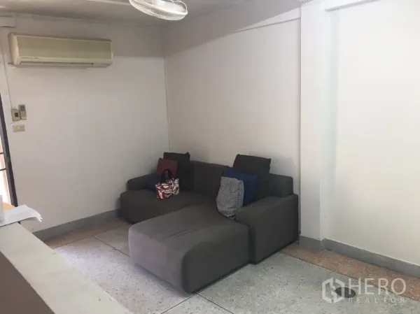 Townhouse for rent in Khlong Toei, Bangkok - Compact living area with gray sofa and wall air conditioner.