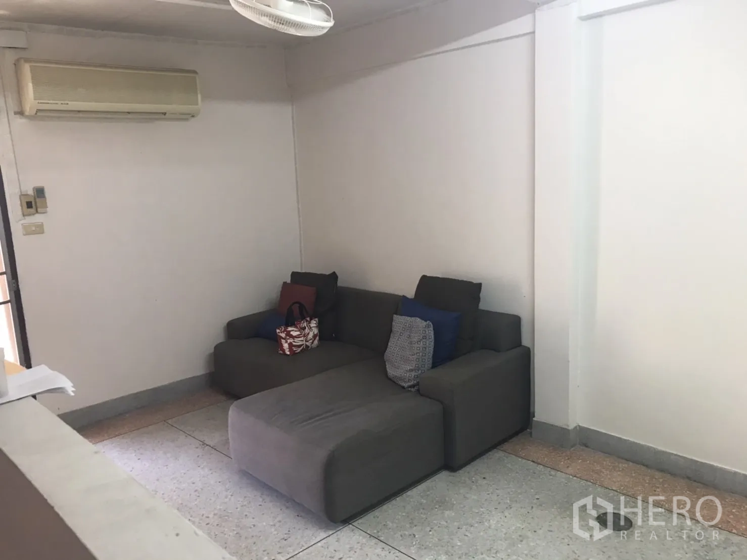 Townhouse for rent in Khlong Toei, Bangkok - Compact living area with gray sofa and wall air conditioner.