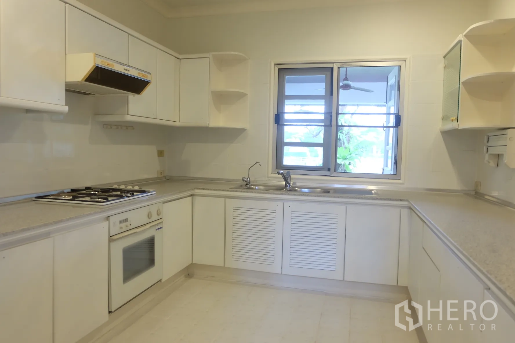 独立式住宅 出租在Bang Phli, Samut Prakan - 明亮的U形厨房，白色橱柜，燃气灶、嵌入式烤箱与窗户。