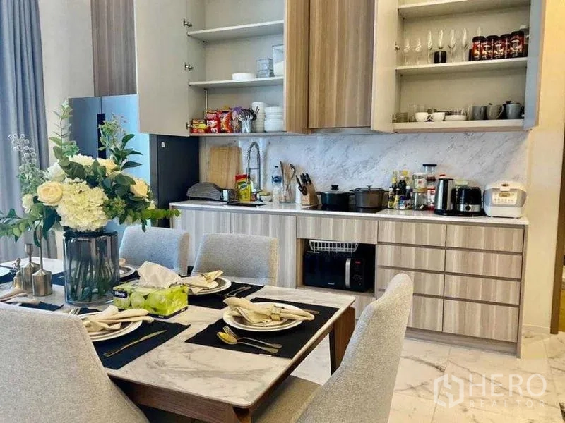 公寓 出售 - 近景展示现代厨房橱柜、大理石挡板与已摆盘的餐桌。