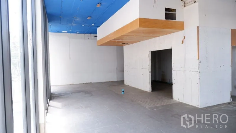 零售空间 出租在Watthana, Bangkok - 开放式零售区，整面玻璃立面与悬挂木质吊顶，蓝色天花。