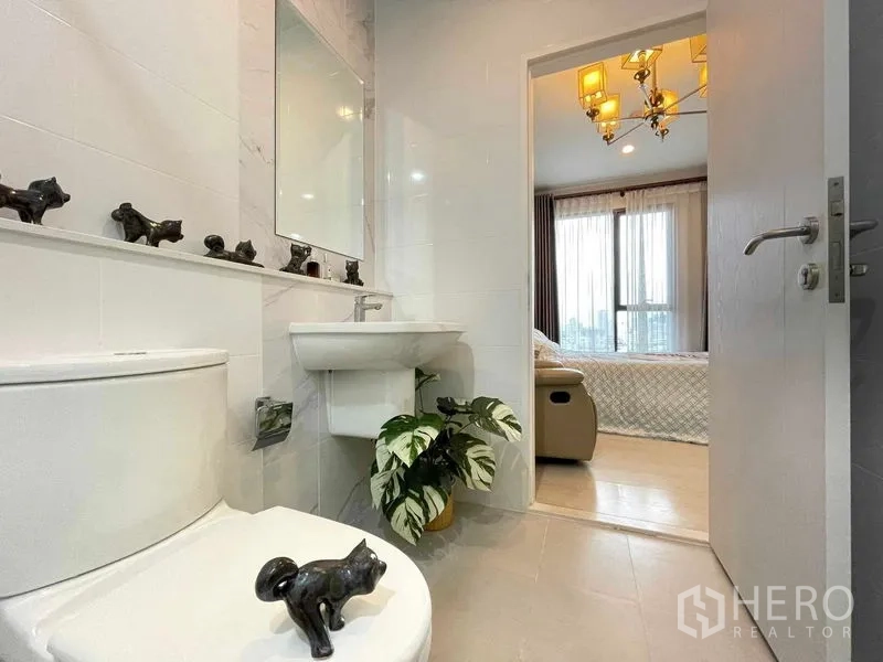 Condominium for sale in Huai Khwang, Bangkok - Clean bathroom with large mirror and indoor plant, opening toward the bedroom.