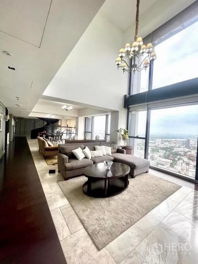 Condominium for rent in Sathon, Bangkok - Open-plan lounge with large sectional, marble floors and panoramic Bangkok views through tall glass walls.