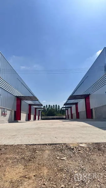 货栈 出租在Khlong Sam Wa, Bangkok - 两侧仓库之间的中轴车道，红色装卸门与雨棚，蓝天之下。