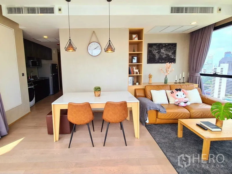 Condominium for rent in Bang Rak, Bangkok - Bright open-plan living and dining area with leather sofa, dining table, built-in shelving and large windows overlooking Bangkok.