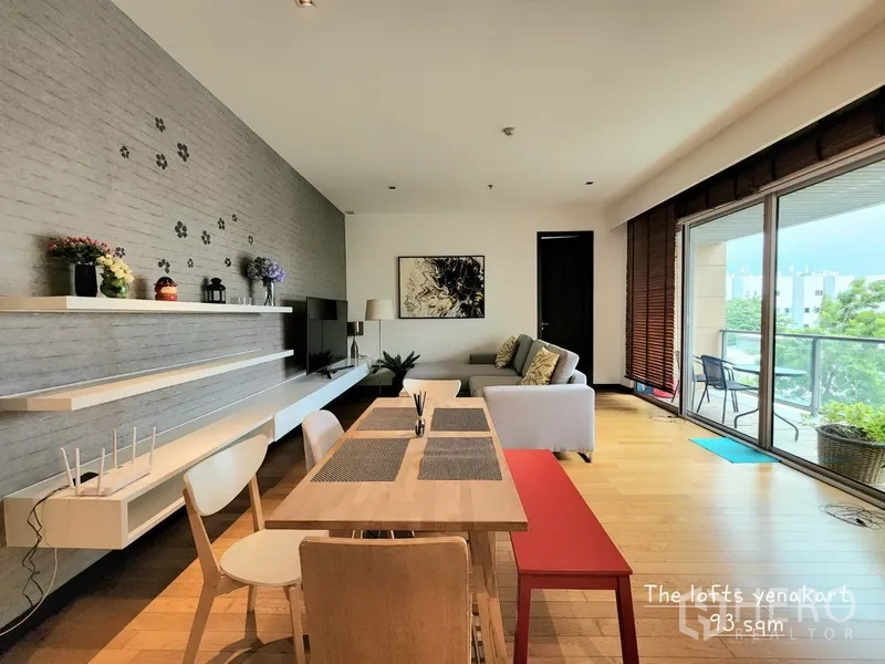 Condominium for rent in Yan Nawa, Bangkok - Open-plan living and dining room in a Yan Nawa Bangkok condo with wood flooring, wall shelves, and a large balcony overlooking greenery.