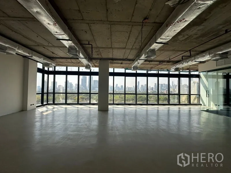 Office Space for rent in Watthana, Bangkok - Spacious shell office showing exposed ductwork ceiling, a central column and wraparound windows with skyline views.