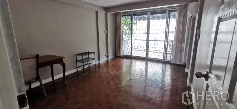 Townhouse for rent in Watthana, Bangkok - Spacious living room with parquet floors and sliding doors to a balcony with security grilles