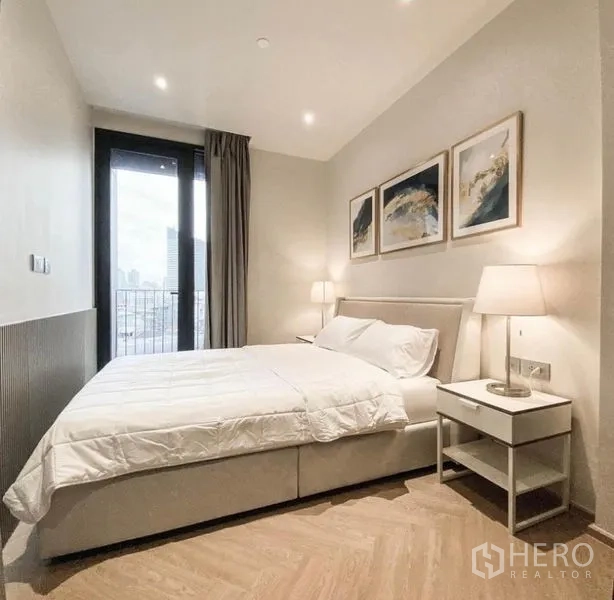 Condominium for rent in Din Daeng, Bangkok - Light bedroom with double bed, bedside lamps and a door to the balcony area with city view.