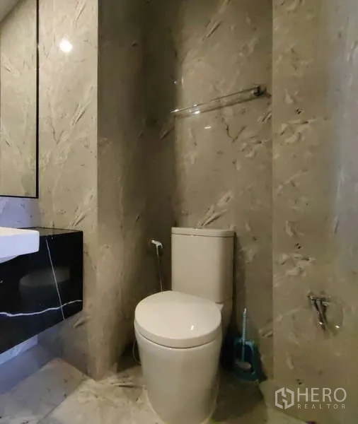 Condominium for rent in Watthana, Bangkok - Modern bathroom with marble tiles, toilet, and a floating black vanity with mirror.