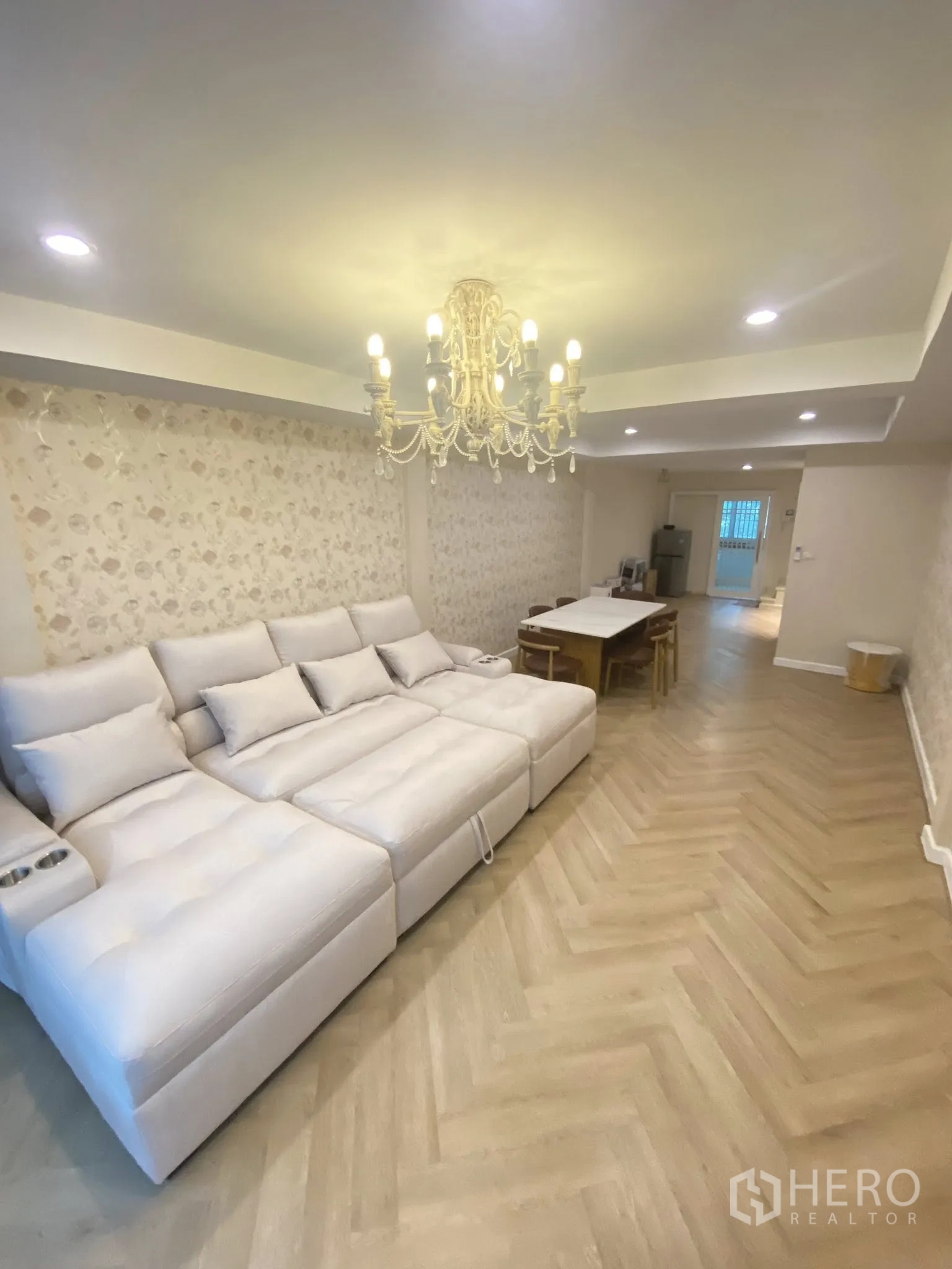 Home Office for rent in Pathum Wan, Bangkok - Open‑plan living and dining area with herringbone floors, chandelier, and a large sectional sofa.