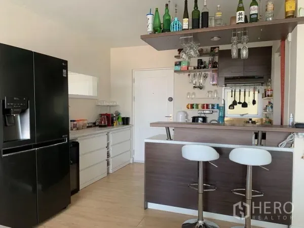 คอนโด ให้เช่าในBang Na, Bangkok - ครัวเปิดพร้อมเคาน์เตอร์บาร์ เก้าอี้สตูล ชั้นแขวนแก้ว และตู้บิวท์อินไม้โทนเข้ม