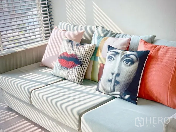 คอนโด ให้เช่าในWatthana, Bangkok - ภาพระยะใกล้ของโซฟาพร้อมหมอนลายกราฟิกสีสัน ข้างหน้าต่างบานเกล็ด