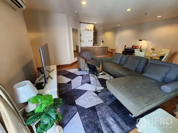 Condominium for rent in Huai Khwang, Bangkok - Spacious open-plan living room with L-shaped sofa, TV console and patterned rug on wooden floors.
