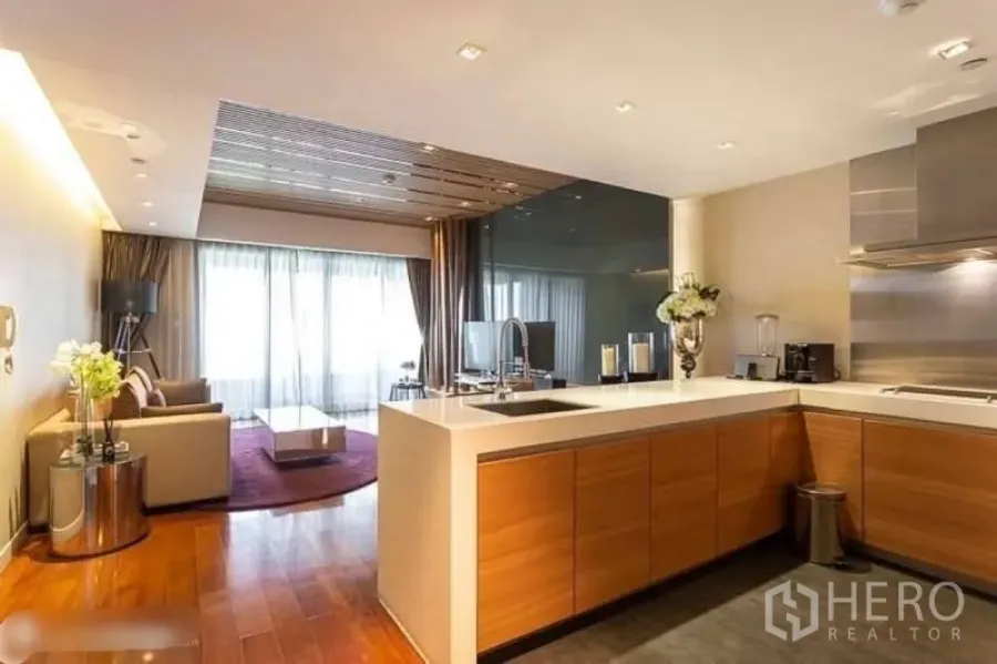 Condominium for rent in Yan Nawa, Bangkok - Open‑plan living area with bright glass doors and a modern island kitchen featuring wood cabinetry and stone counters.