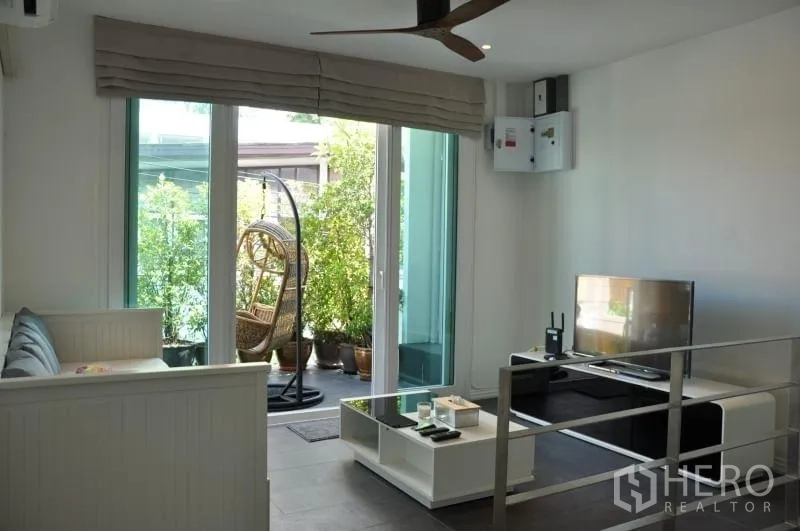 Townhouse for rent or sale in Watthana, Bangkok - Upstairs lounge with TV, ceiling fan and balcony featuring a hanging chair and potted plants.