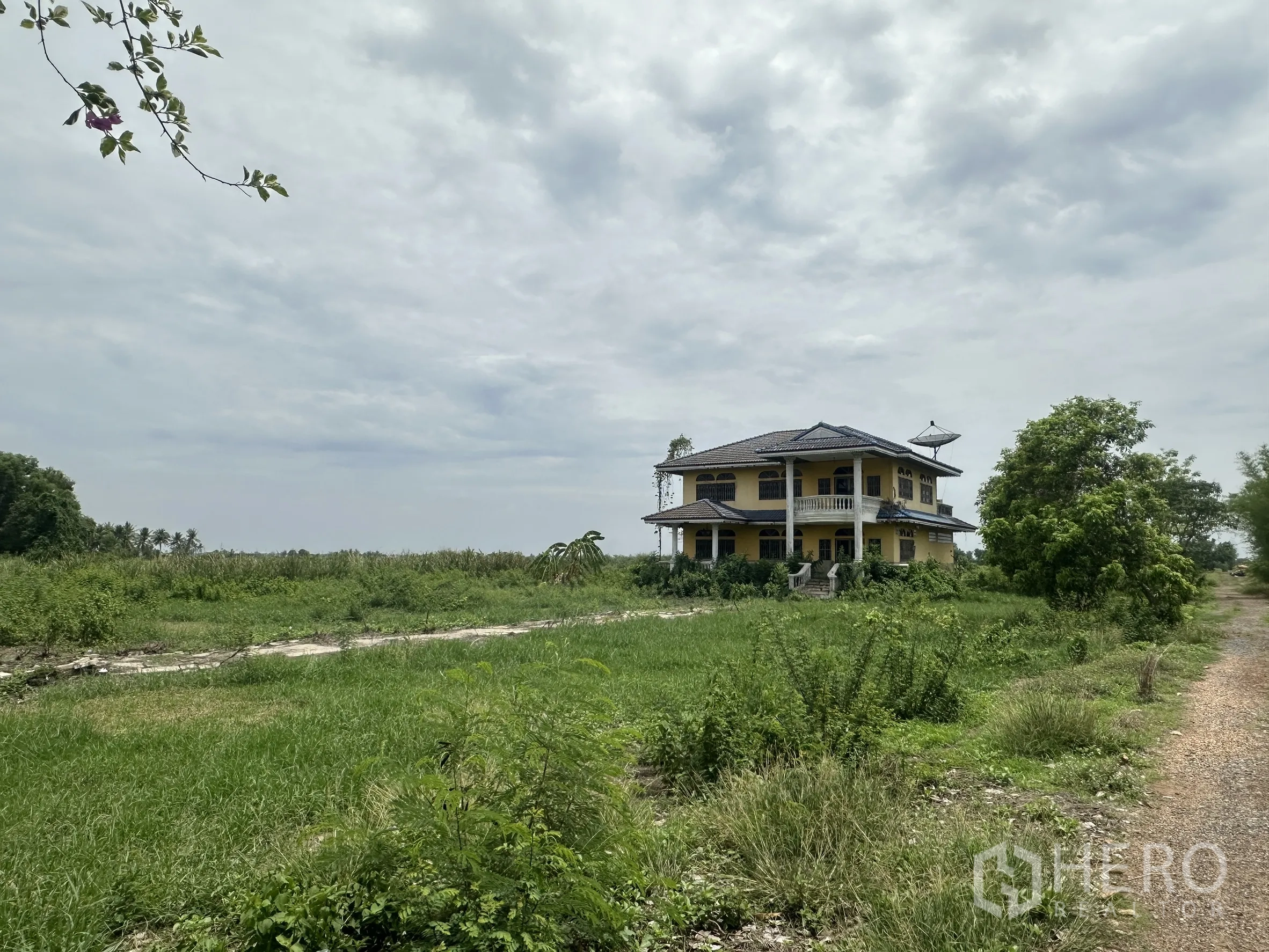 Land for sale in Bang Nam Priao, Chachoengsao - Wide field with a distant house and an unpaved access road.