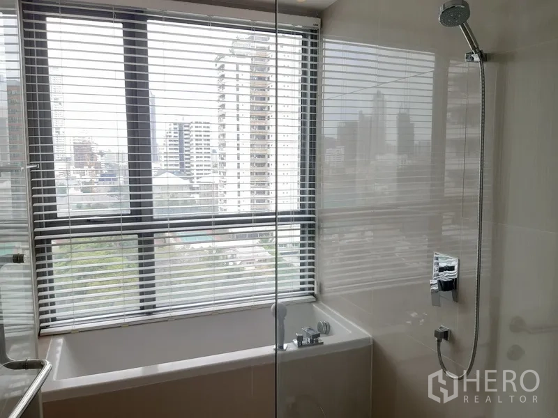 คอนโด ให้เช่าในWatthana, Bangkok - ห้องน้ำมีอ่างอาบน้ำกั้นกระจกพร้อมฝักบัว ข้างหน้าต่างบานกว้างและวิวตึกเมือง
