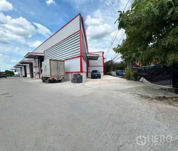 货栈 出租在Sai Mai, Bangkok - 仓库侧面宽阔车道，金属外墙，卡车进出与调头空间充足。