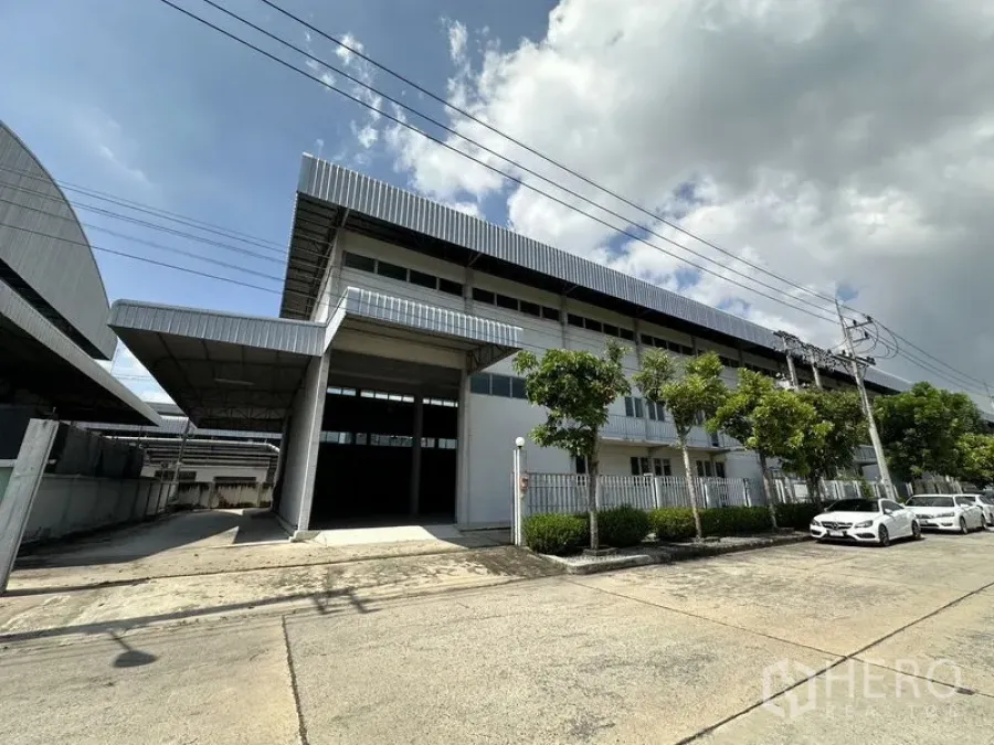 工厂 出租在Lam Luk Ka, Pathum Thani - 现代化工厂外观，带大尺度雨棚装卸口与围栏门，临静谧街道。