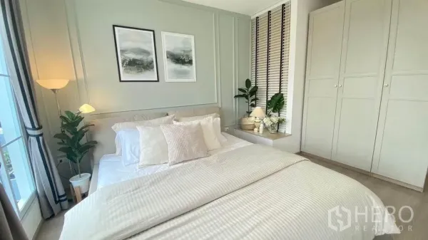Townhouse for rent in Prawet, Bangkok - Serene bedroom with panelled feature wall, crisp white bedding, floor lamp, built-in wardrobe and potted plants.