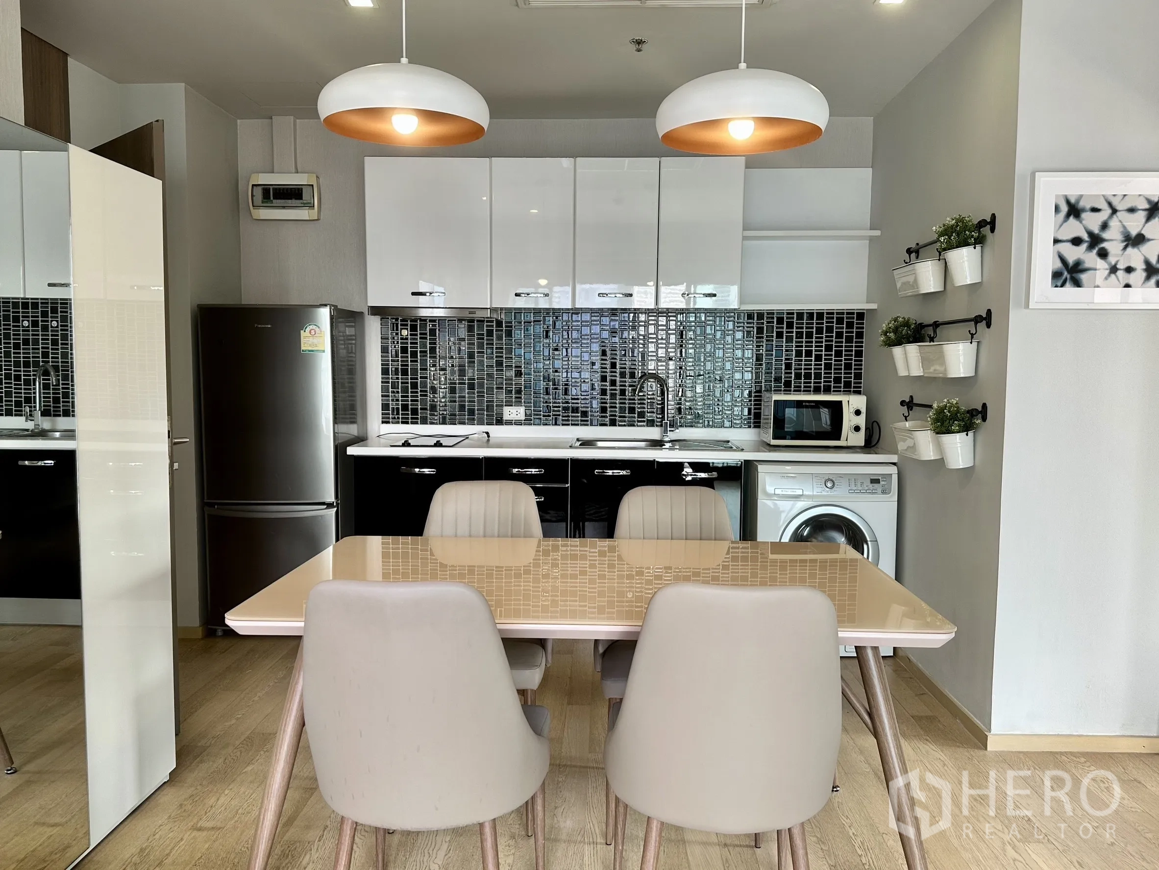 Condominium for rent in Bangkok - Modern kitchenette with glossy cabinets, mosaic backsplash, fridge, microwave and in-unit washer next to a four-seat dining set.