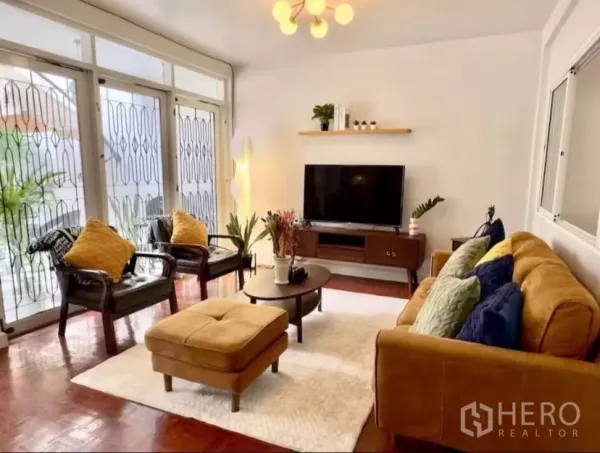 Townhouse for rent in Watthana, Bangkok - Living area facing large windowed doors with security grills, rug and ottoman.