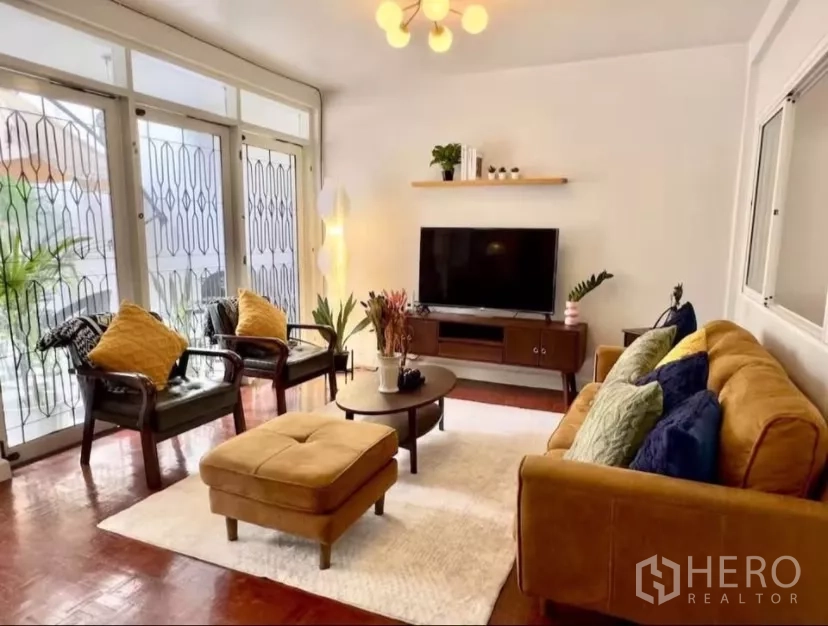 Townhouse for rent in Watthana, Bangkok - Living area facing large windowed doors with security grills, rug and ottoman.