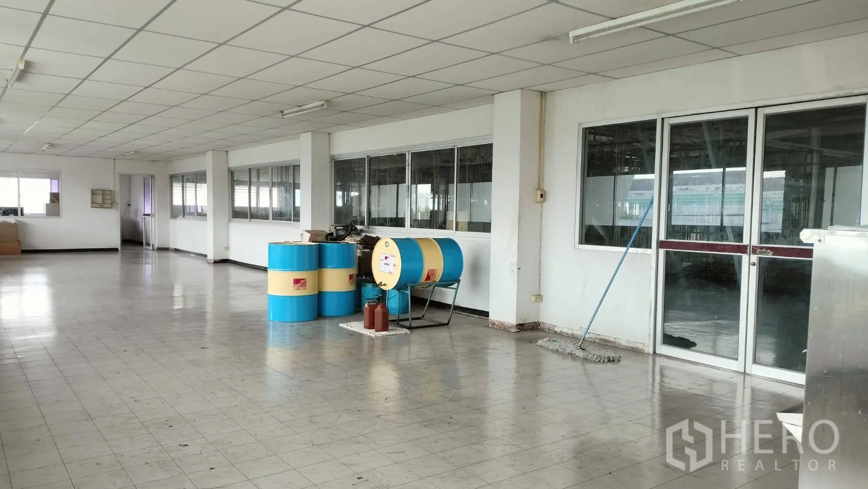 Factory for rent in Lat Krabang, Bangkok - Tiled mezzanine office area with glass partitions, sliding door, and storage drums.