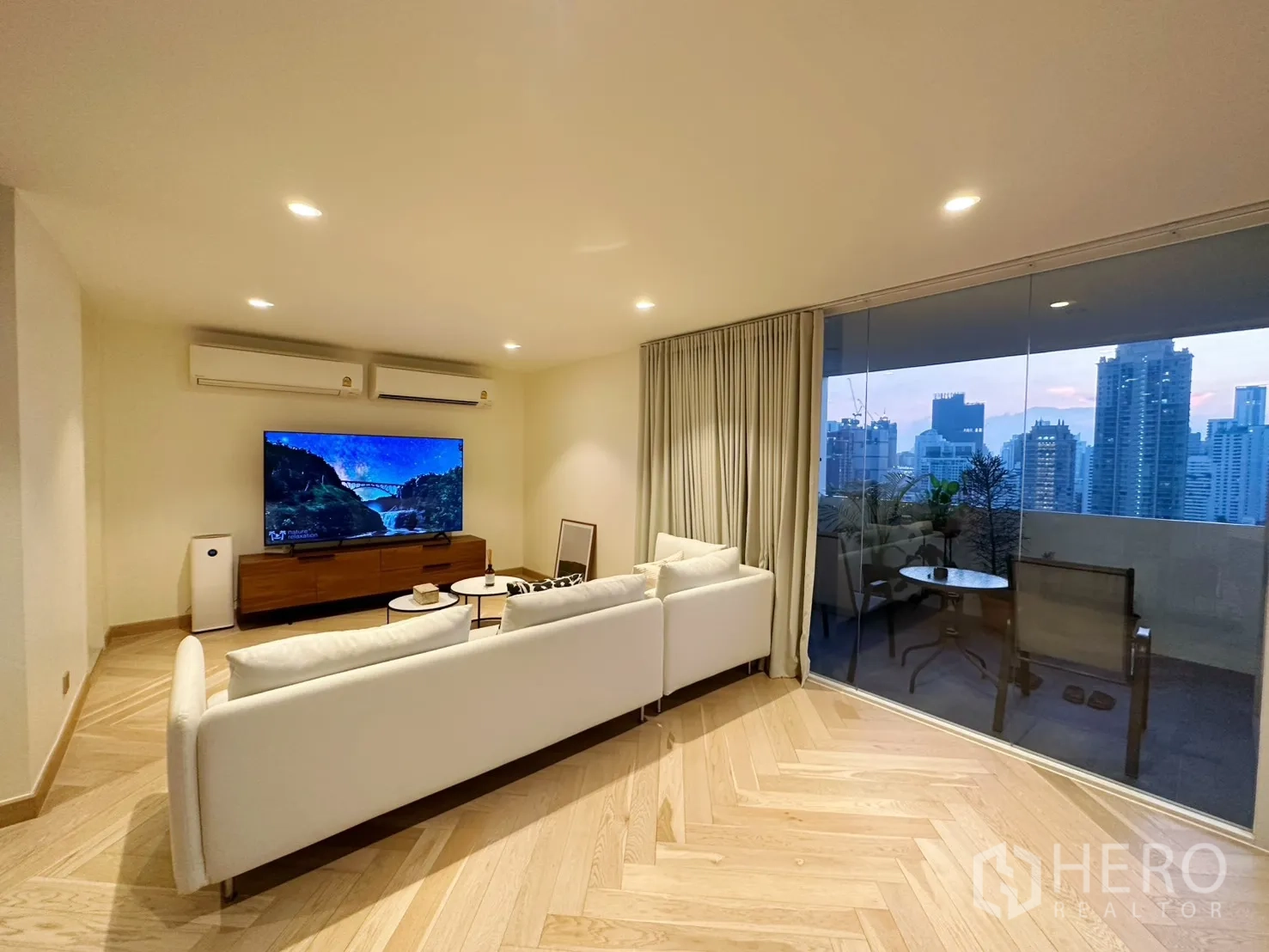 Condominium for rent or sale in Watthana, Bangkok - Living room facing a large TV and balcony with floor-to-ceiling glass and city views.