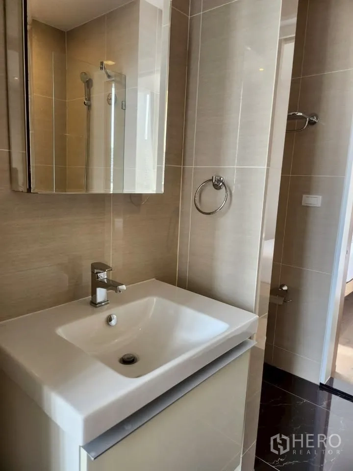 Condominium for rent in Khlong Toei, Bangkok - Contemporary bathroom with beige tiles, vanity sink and mirrored cabinet.