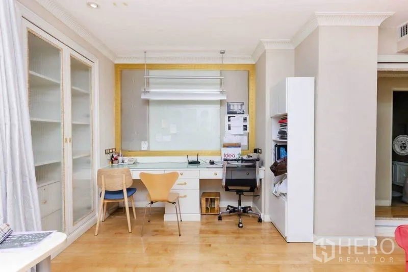 Condominium for rent or sale in Pathum Wan, Bangkok - Home office area with wall-to-wall desk, storage cabinets, and light wood floors.