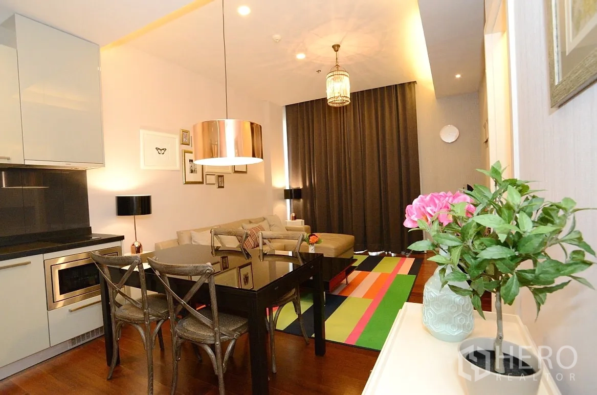 Condominium for rent in Watthana, Bangkok - Open-plan living room with modern kitchenette, pendant lights, glass dining table, and a colorful rug in a Thonglor condo.