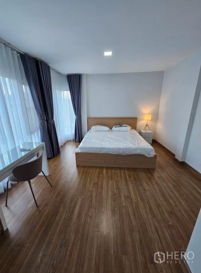 Detached House for rent in Bang Phli, Samut Prakan - Spacious master bedroom with bed, work desk, corner windows and wood flooring.