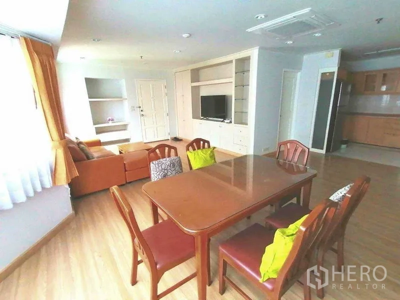 Condominium for rent in Watthana, Bangkok - Dining area facing built-in TV wall and shelving, open to living room and kitchen.