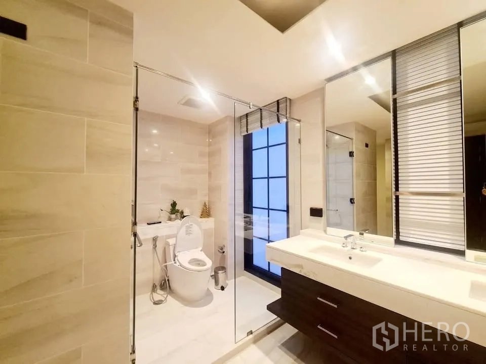 Townhouse for rent or sale in Watthana, Bangkok - Contemporary bathroom with glass shower enclosure, toilet, and large mirror.
