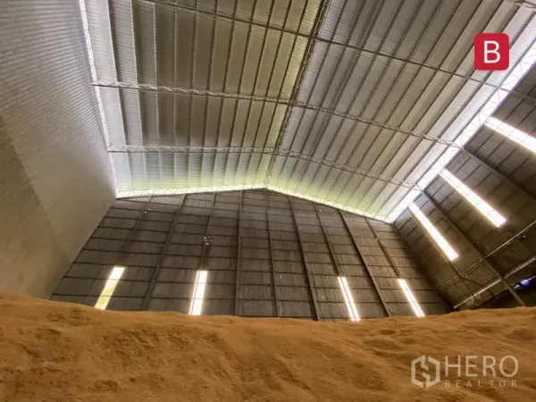 工厂 出租在Chachoengsao - 近景高金属屋顶与竖向采光带，前景为散装原料堆。