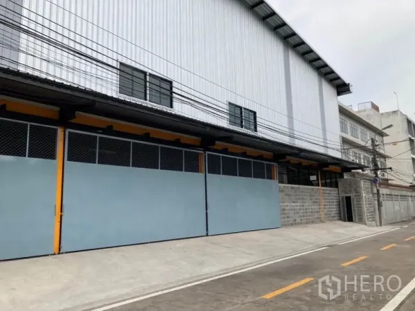 货栈 出租在Khlong Toei, Bangkok - 仓库外立面，长条金属滑动门与波纹钢板墙，临街通道