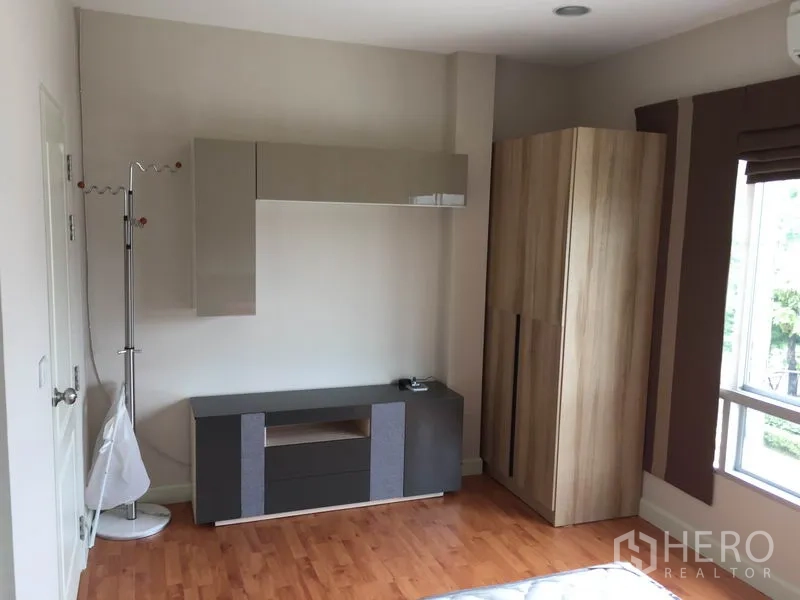 Detached House for rent or sale in Saphan Sung, Bangkok - Bright secondary bedroom with wood floor, wardrobe and wall-mounted storage cabinet.