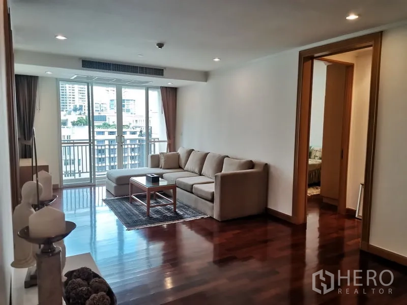 公寓 出租在Khlong Toei, Bangkok - 客厅设L型沙发与茶几，推拉门通向可观城市景致的阳台。