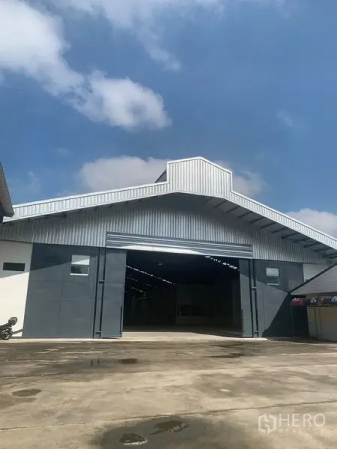 Warehouse for rent in Phra Pradaeng, Samut Prakan - Modern gable‑roof warehouse facade with wide roller shutter and expansive concrete truck yard in Phra Pradaeng.