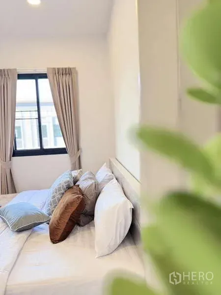 Townhouse for rent in Min Buri, Bangkok - Bright bedroom with double bed, neutral curtains and a window letting in natural light.