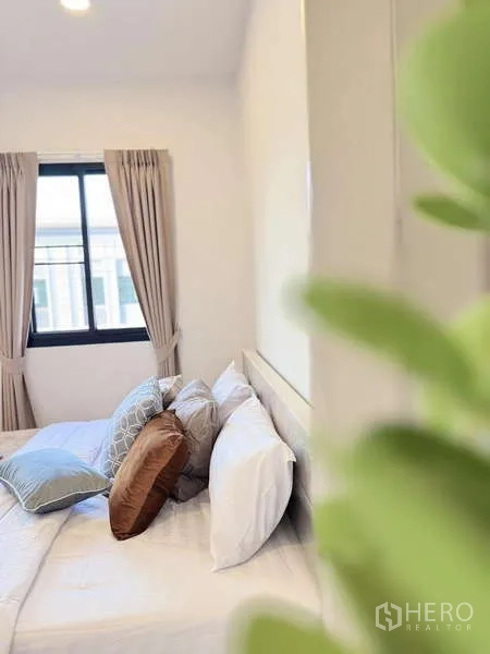 Townhouse for rent in Min Buri, Bangkok - Bright bedroom with double bed, neutral curtains and a window letting in natural light.