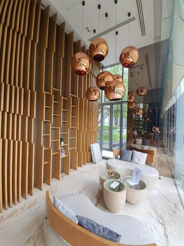 Condominium for rent in Watthana, Bangkok - Double‑height lobby featuring a sculptural wooden wall and copper pendant lights.