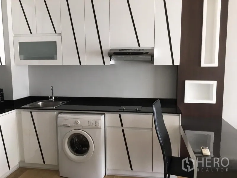 คอนโด ให้เช่าในBangkok - ครัวบิลท์อินสีขาว เคาน์เตอร์หินสีดำ เตาและเครื่องดูดควัน พร้อมเครื่องซักผ้าฝาหน้า