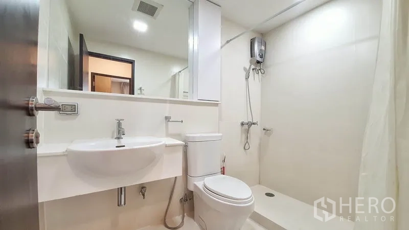 公寓 出租在Khlong Toei, Bangkok - 现代白色卫浴，挂墙式洗手台、坐便器与带热水器的步入式淋浴间。