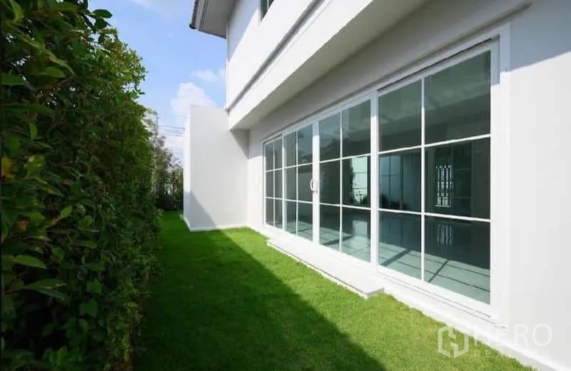 Detached House for rent or sale in Bang Phli, Samut Prakan - Side yard with sliding glass doors opening to lawn and hedge.