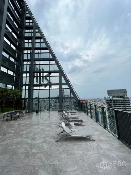 Condominium for rent in Bang Rak, Bangkok - Rooftop terrace with lounge chairs and glass facade overlooking Bangkok skyline.